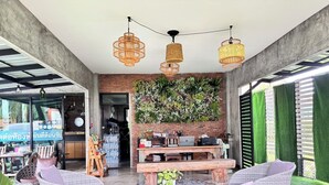 A modern interior with wicker furniture, a brick wall, and a green wall with plants. - Le Park 23 Boutique Resort (Roi Et)