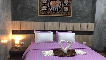 A neatly made bed with a heart-shaped towel arrangement, a wall-mounted decorative piece, and a bedside lamp.