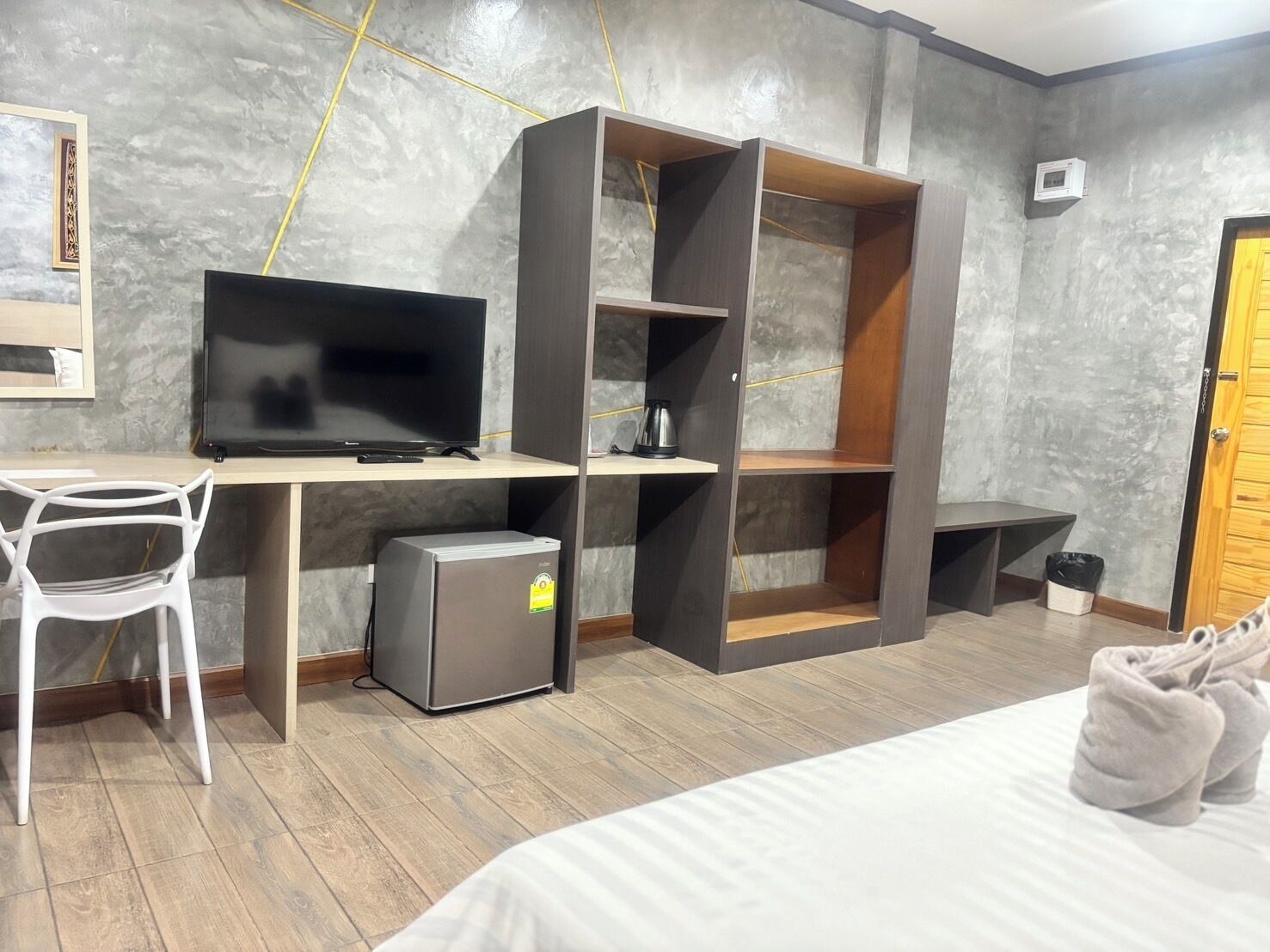 A modern room with a bed, a desk with a television, a mini-fridge, and built-in shelving.