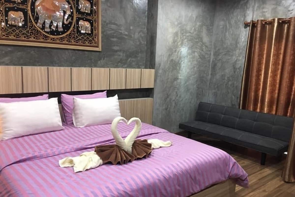 A modern bedroom with a large bed, a headboard, a sofa, and a wall-mounted decorative piece.