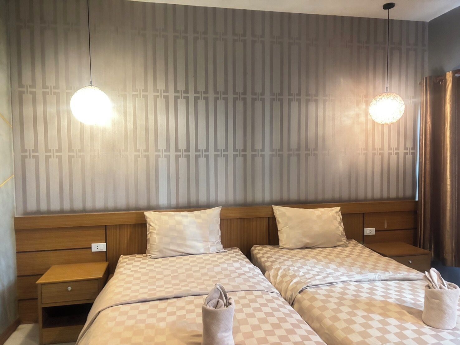 Ett hotellrum med två sängar, trägavlar, rutigt sänglinne och två hängande lampor.