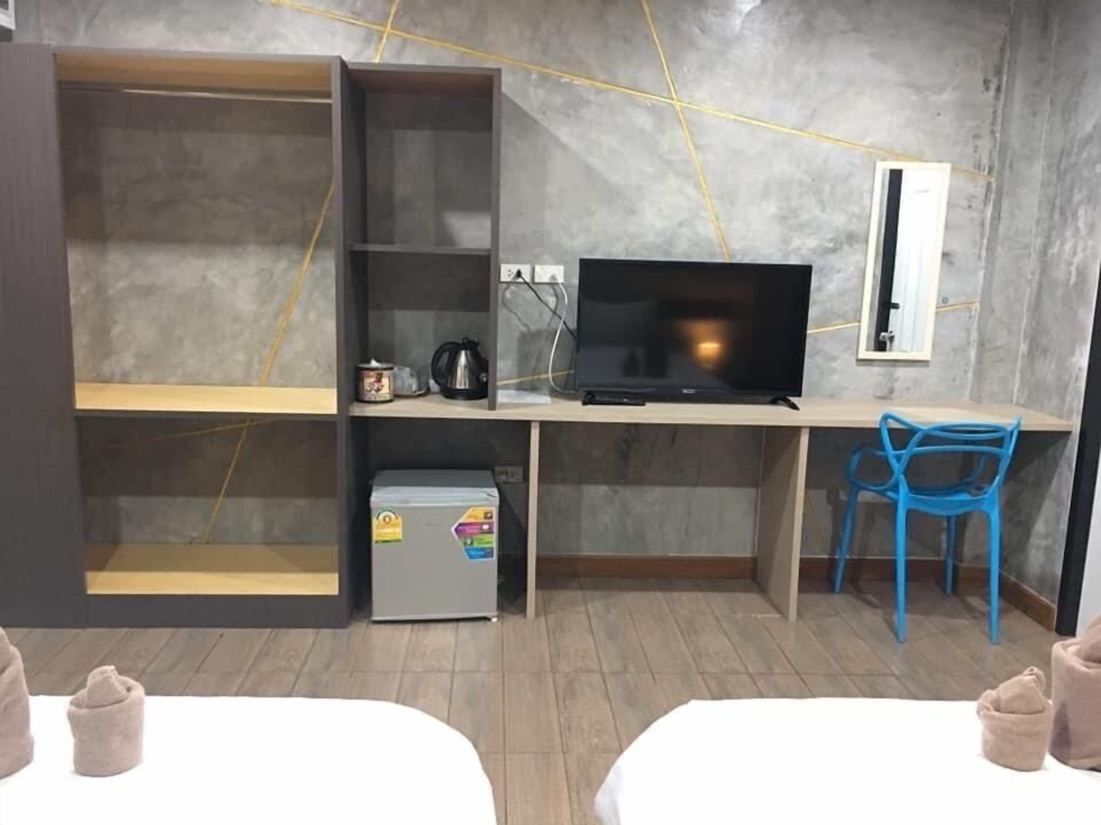 Una habitación con escritorio, televisión, una silla y dos camas.