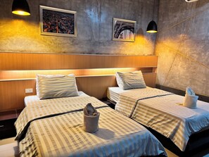 A hotel room with two beds, each with striped bedding and pillows. There are two framed pictures on the wall, one of a cityscape and another of a bridge. The room has a wooden headboard and a wall-mounted light fixture. - Le Park 23 Boutique Resort (Roi Et)