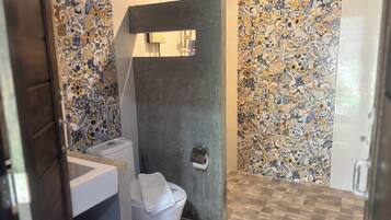 A bathroom with a toilet, a trash bin, and a shower area.