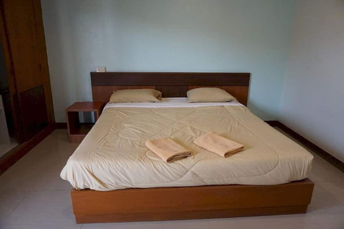 A neatly made bed with a wooden headboard, two pillows, and two rolled towels on the bed.
