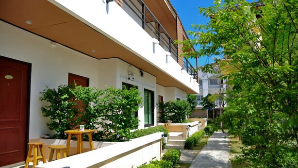 Um edifício residencial com área externa coberta, mobiliário de madeira e vegetação.