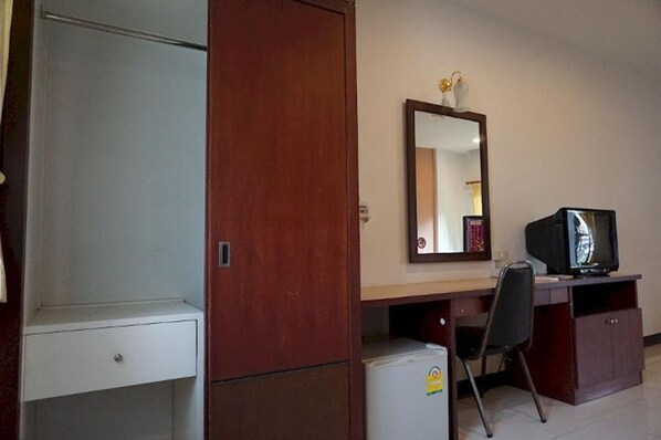 Una habitación pequeña con un armario de madera, un escritorio con silla, televisor y refrigerador.