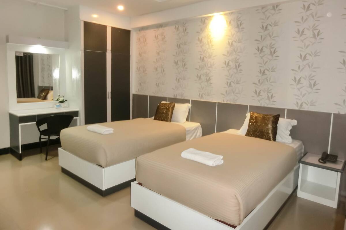 A hotel room with two beds, a desk, a chair, and a nightstand with a phone.