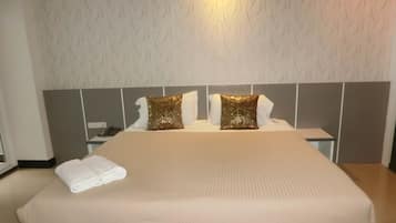 A neatly made bed with a beige bedspread and two decorative pillows, a bedside table with a phone, and a wall with a textured pattern.