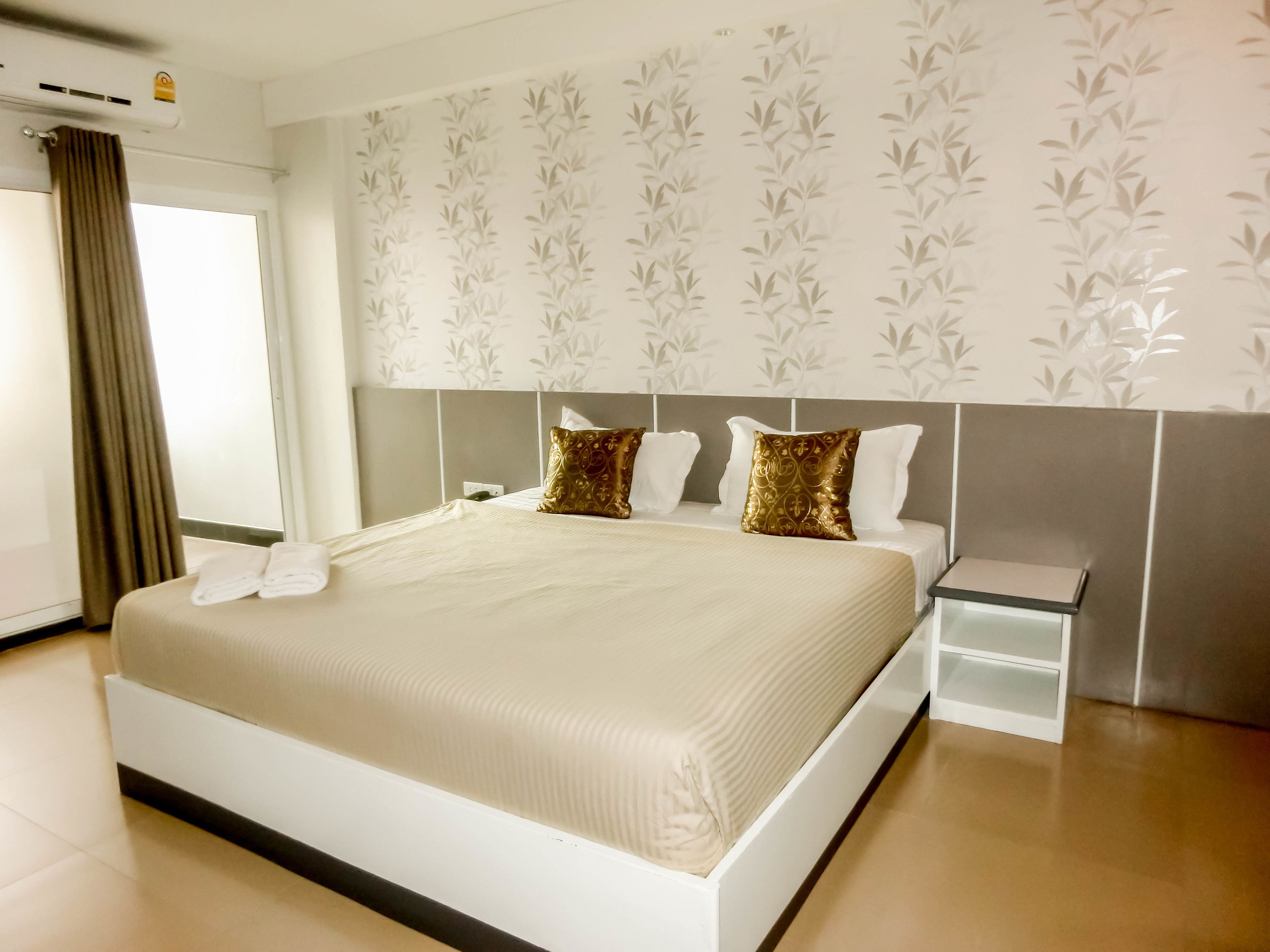 A hotel room with a large bed, a bedside table, and a window with curtains.