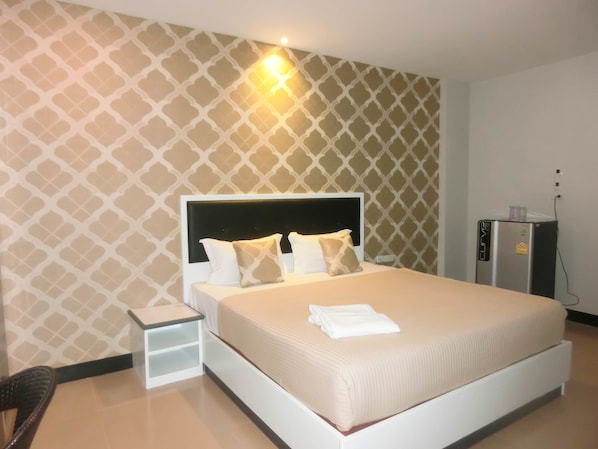 A neatly made bed with white bedding and two pillows, a small bedside table, and a wall-mounted heater. - The Premium Residence (Roi Et)