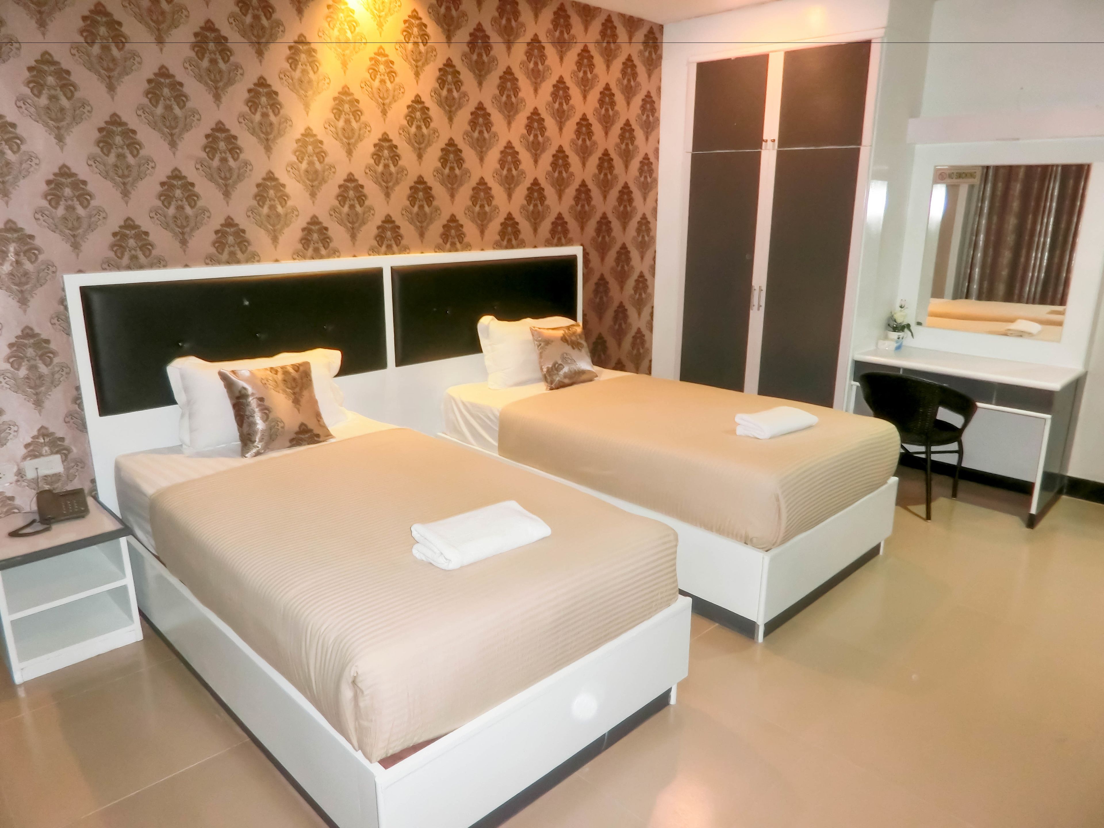 A hotel room with two beds, a desk, and a mirror.