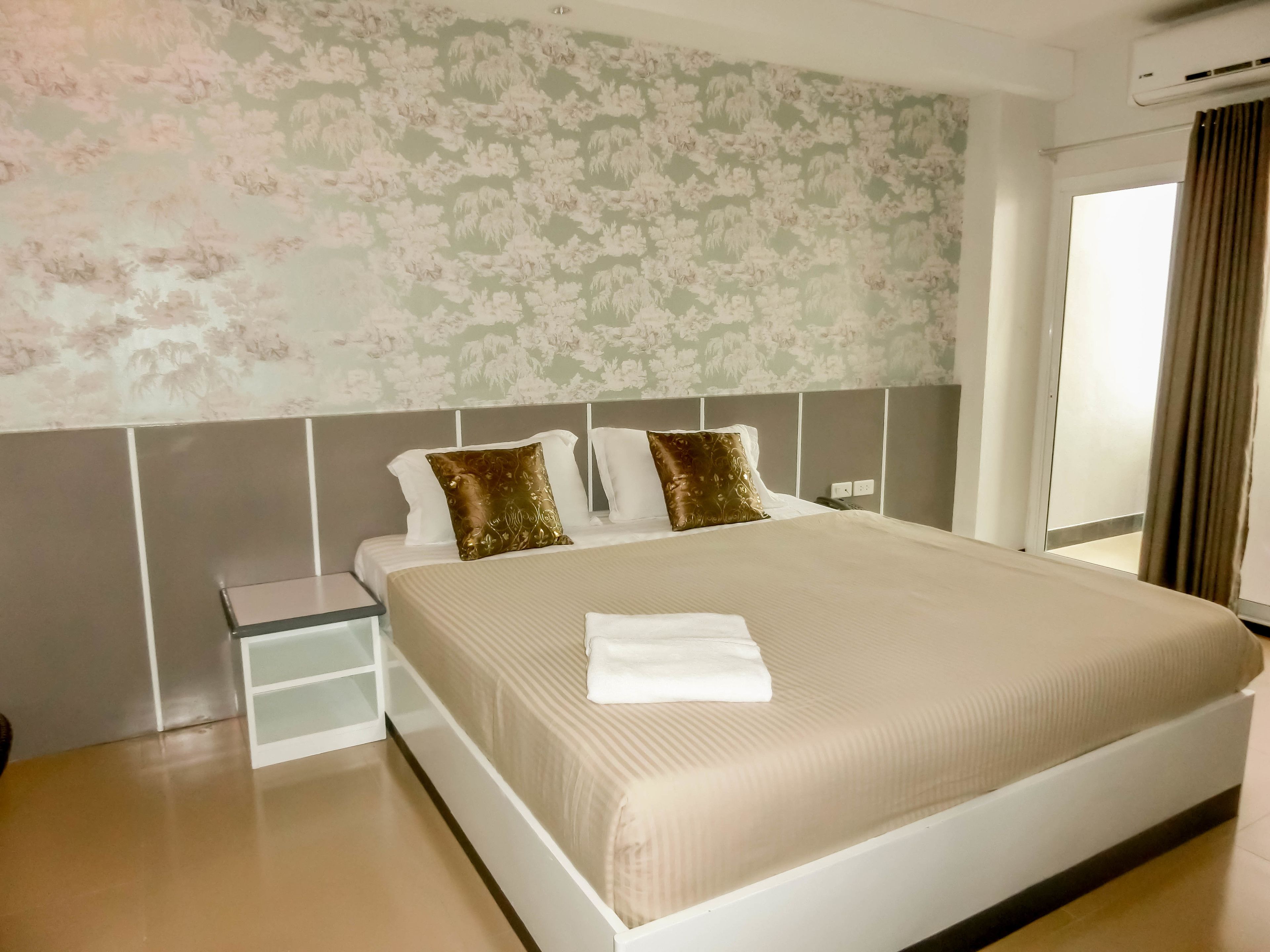 A neatly made bed with a white and beige bedspread, two decorative pillows, and a folded white towel.