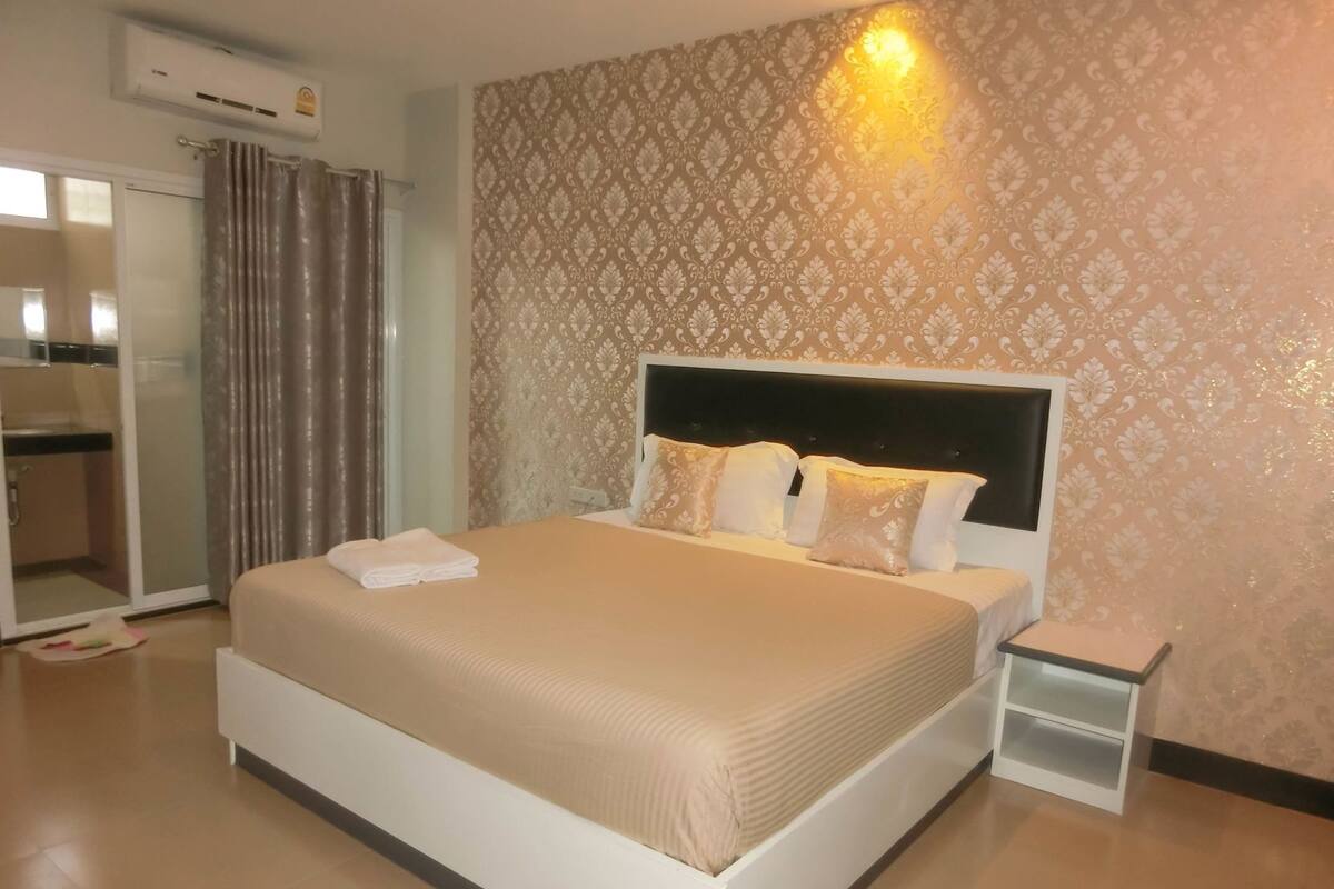 A hotel room with a large bed, a bedside table, a wardrobe, and a shower area.