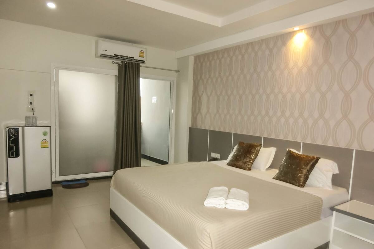 A hotel room with a bed, a nightstand, a minibar, and an air conditioning unit.