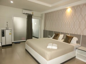 A hotel room with a bed, a nightstand, a minibar, and an air conditioning unit. - The Premium Residence (Roi Et)