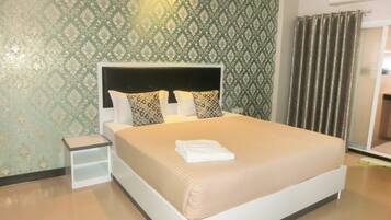 A neatly made bed with a white headboard and multiple pillows, a small bedside table, and a wall with a patterned wallpaper.