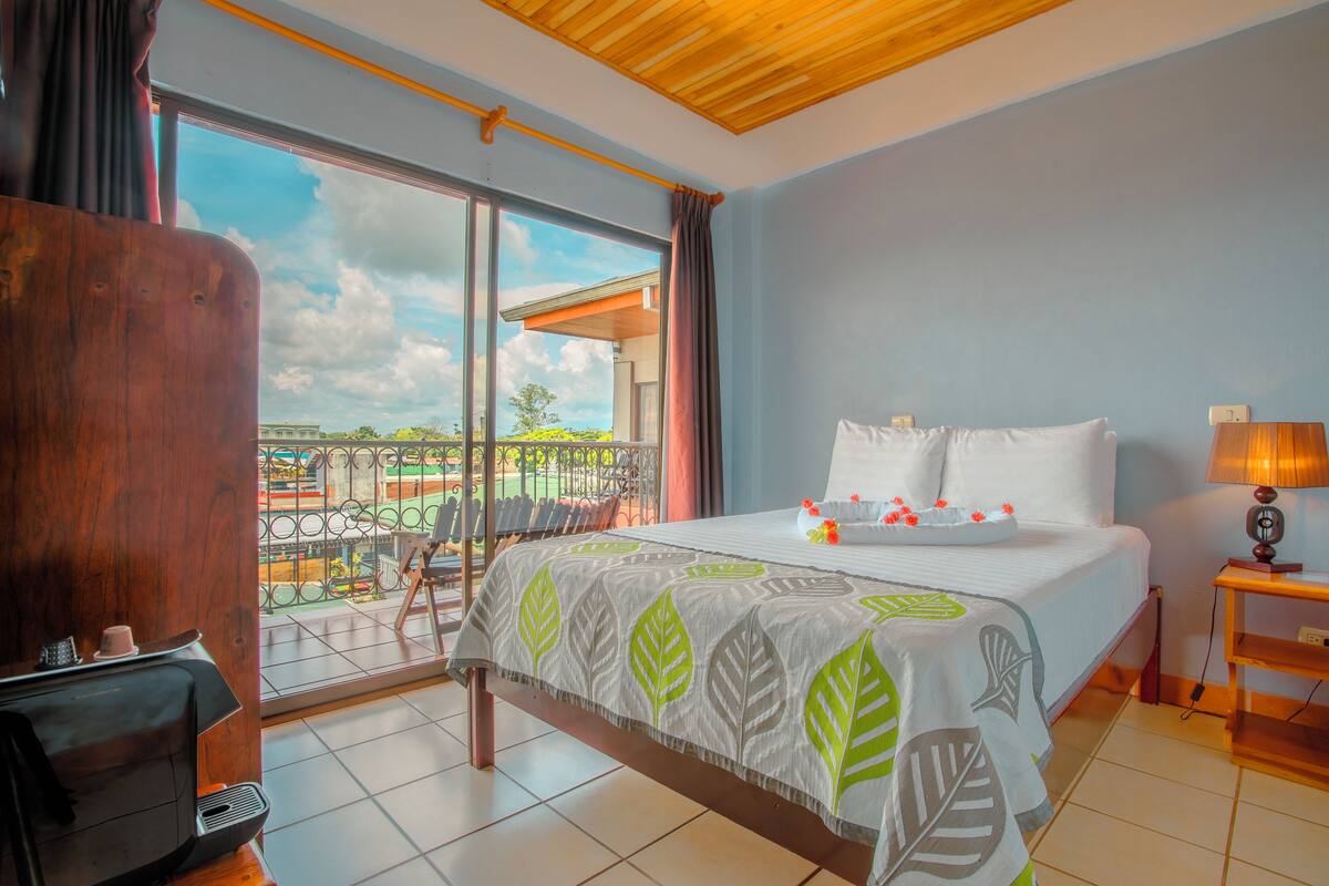 Una camera d'albergo con un letto, una scrivania, una sedia, una lampada e un balcone con vista.