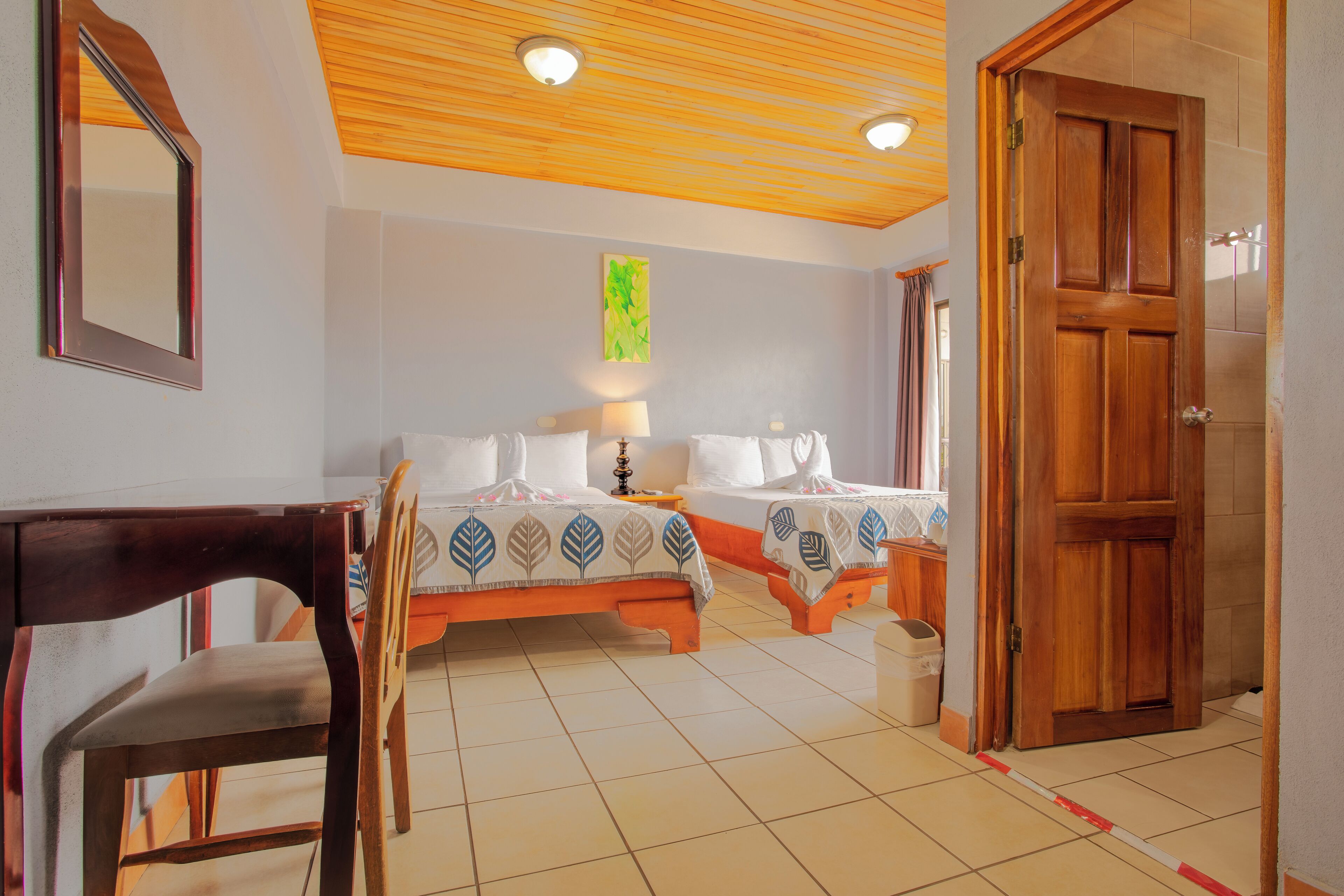Une chambre d’hôtel avec deux lits, un plafond en bois, un miroir et une porte en bois.