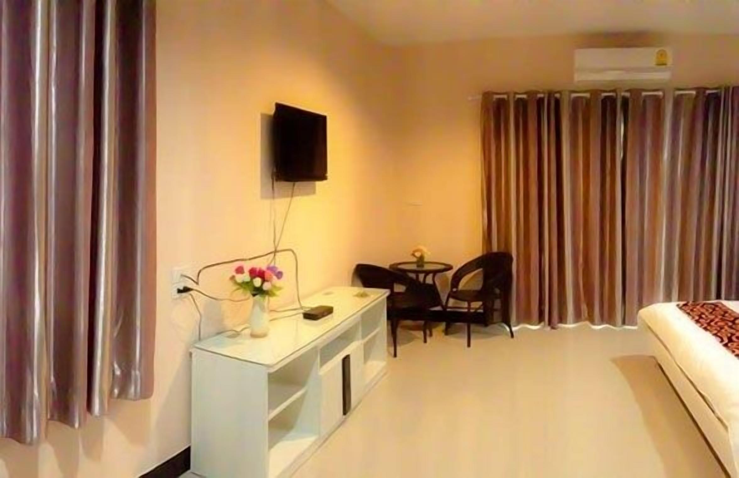 Habitación de hotel con cama, escritorio con silla, televisor montado en la pared y ventana con cortinas.
