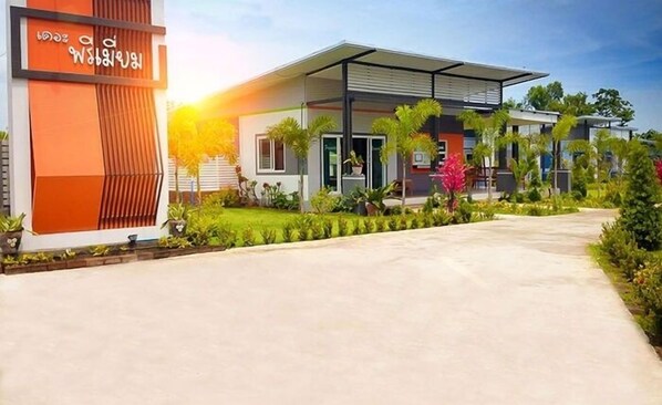A modern building with a covered entrance and a well-maintained garden. - The Premium Resort (Suwannaphum)