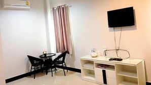 Una habitación pequeña y moderna con un equipo de aire acondicionado blanco, un televisor de pantalla plana montado en la pared, una pequeña mesa consola blanca con un control remoto y un comedor con una mesa redonda pequeña y dos sillas.