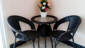Una pequeña mesa redonda con dos sillas negras y una planta en maceta con flores.