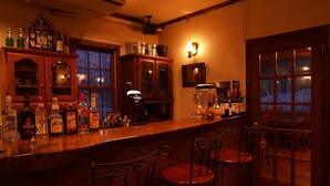 A bar area with wooden chairs, a variety of liquor bottles, and a clock on the wall. - PENSION & TRATTORIA Syo (Hakuba)