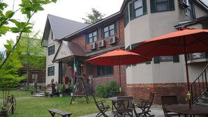 An outdoor patio area with tables and chairs, a swing set, and a brick building with air conditioning units. - PENSION & TRATTORIA Syo (Hakuba)