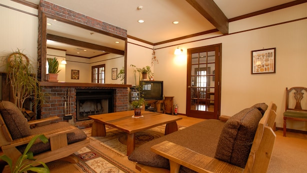 A cozy living room with a fireplace, comfortable seating, and a television. - PENSION & TRATTORIA Syo (Hakuba)