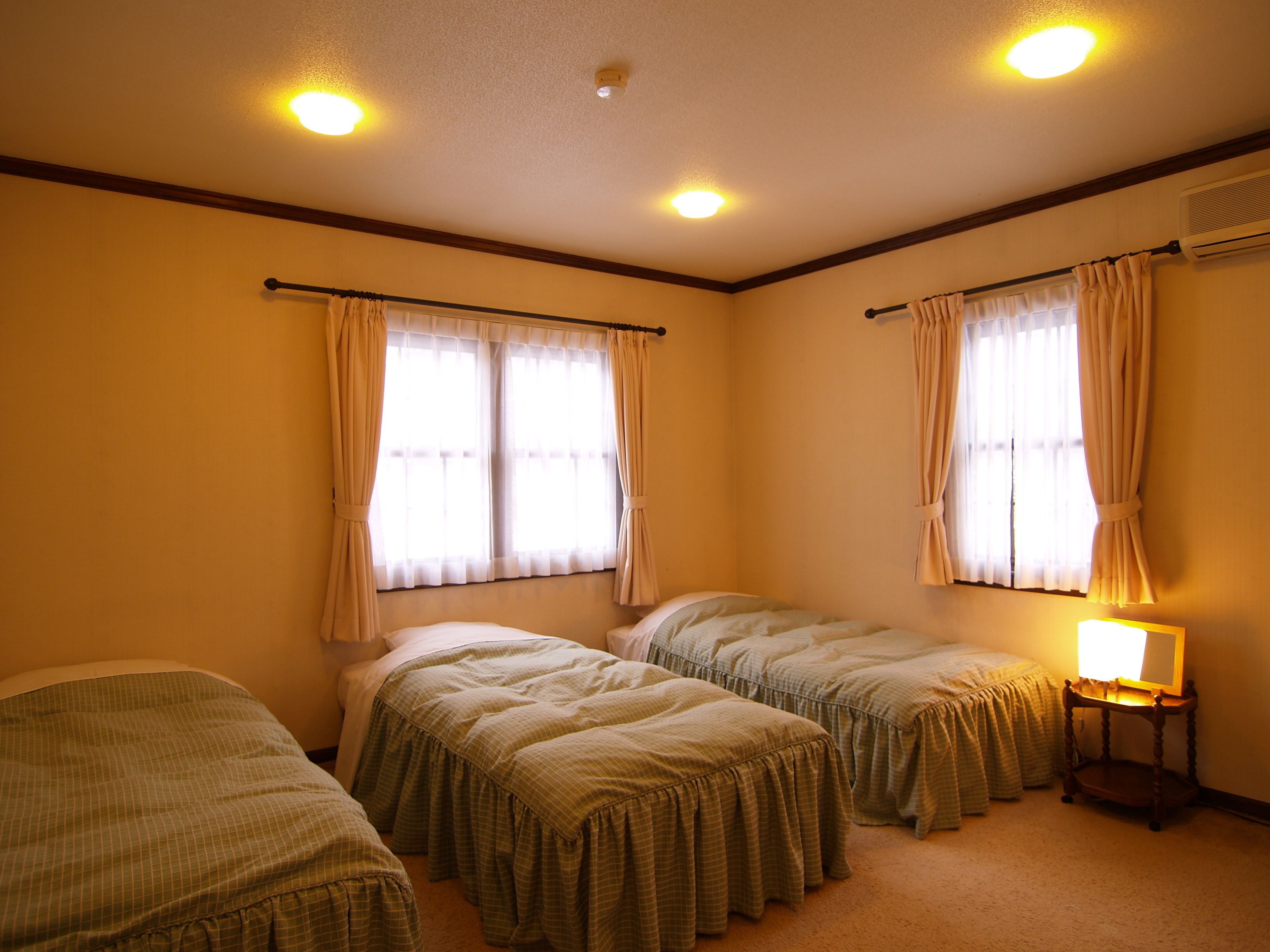 A room with two single beds, a nightstand with a lamp, and a window with curtains.