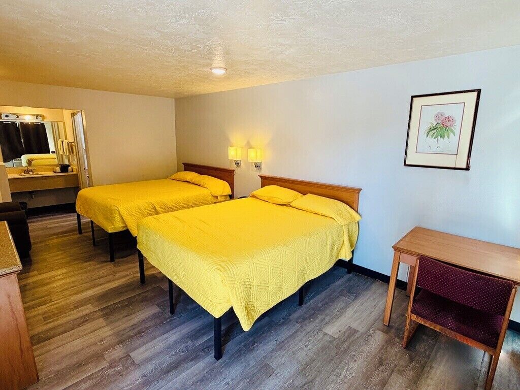 A hotel room with two beds, a wooden desk, a mirror, and a framed picture on the wall.