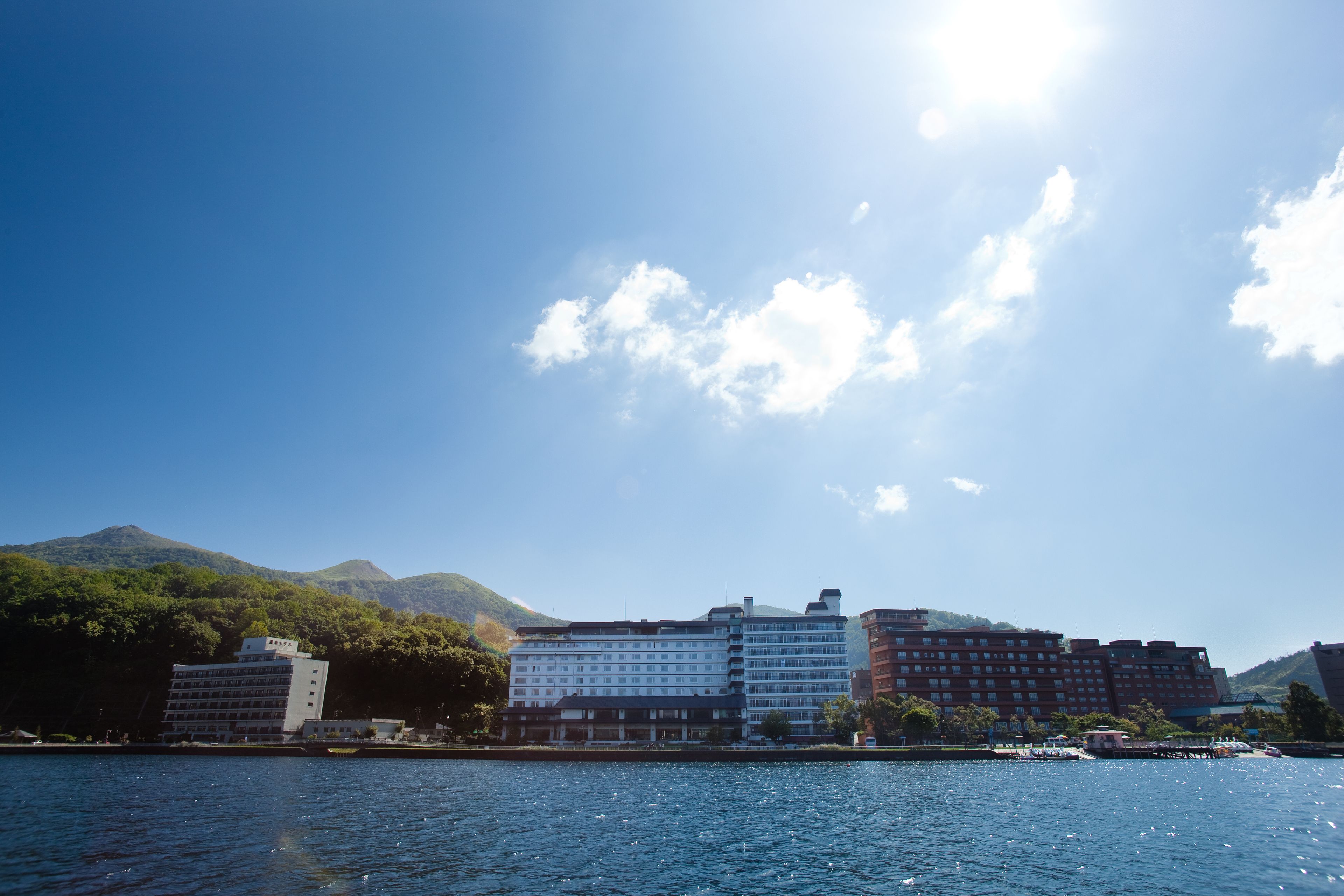 A waterfront hotel with multiple buildings, a clear sky, and mountains in the background.