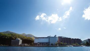 A waterfront hotel with multiple buildings, a clear sky, and mountains in the background.