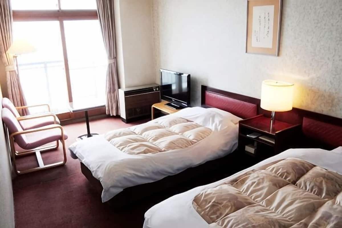 A hotel room with two beds, a TV, a desk, a chair, and a window.