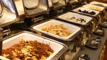 Un bufé con diversas opciones de comida, incluyendo fideos, papas fritas y otros platos, en bandejas de metal.