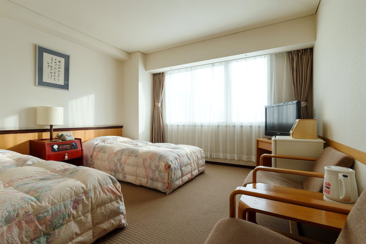 A hotel room with two beds, a TV, a coffee maker, and a bedside table.