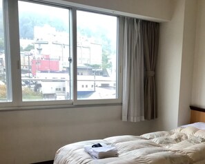 A hotel room with a large window, a bed with a white comforter, and a neatly folded towel on the bed. - Toya Kohantei (Toyako)