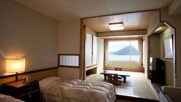 A hotel room with a bed, a desk, a chair, a table, a lamp, a telephone, and a window with a view of a mountain.