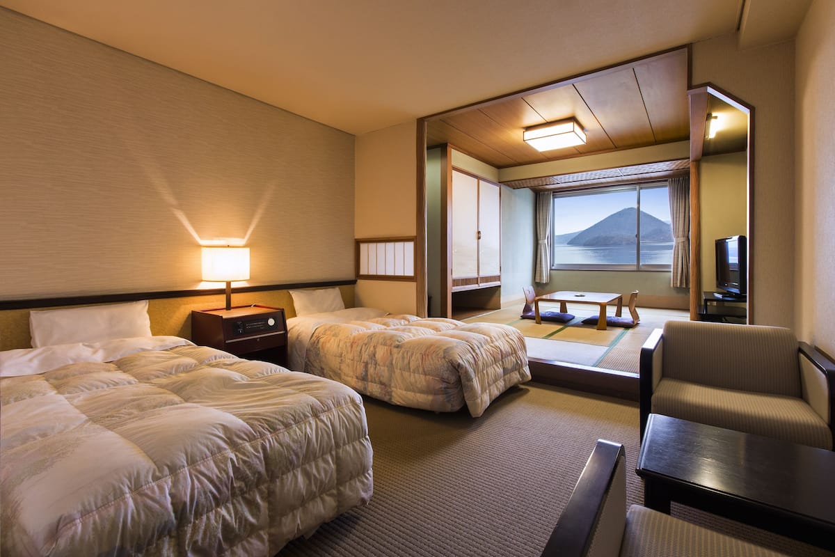 A hotel room with two beds, a seating area, a view of the sea, and a traditional Japanese interior.