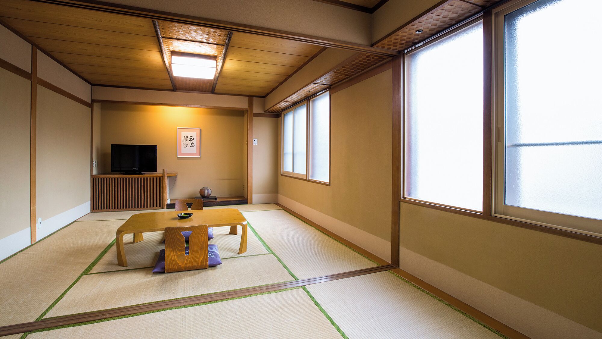 Um quarto japonês tradicional com tatames, uma mesa baixa, uma televisão e portas deslizantes.
