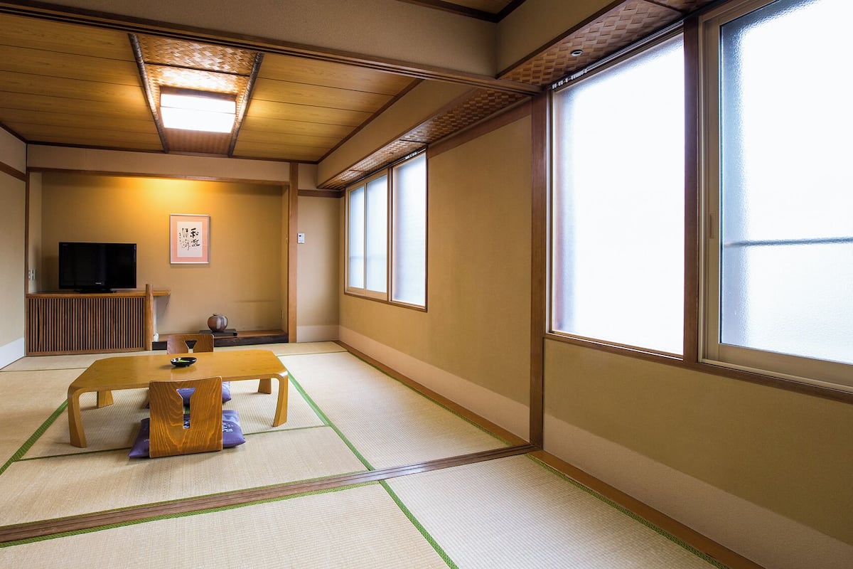 A traditional Japanese room with tatami flooring, a low table, a television, and sliding doors.