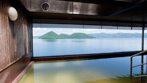 Un interior moderno con un ventanal grande que da a una masa de agua tranquila y colinas verdes.