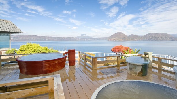 Una terraza de madera con jacuzzis y vistas a un lago y montañas.