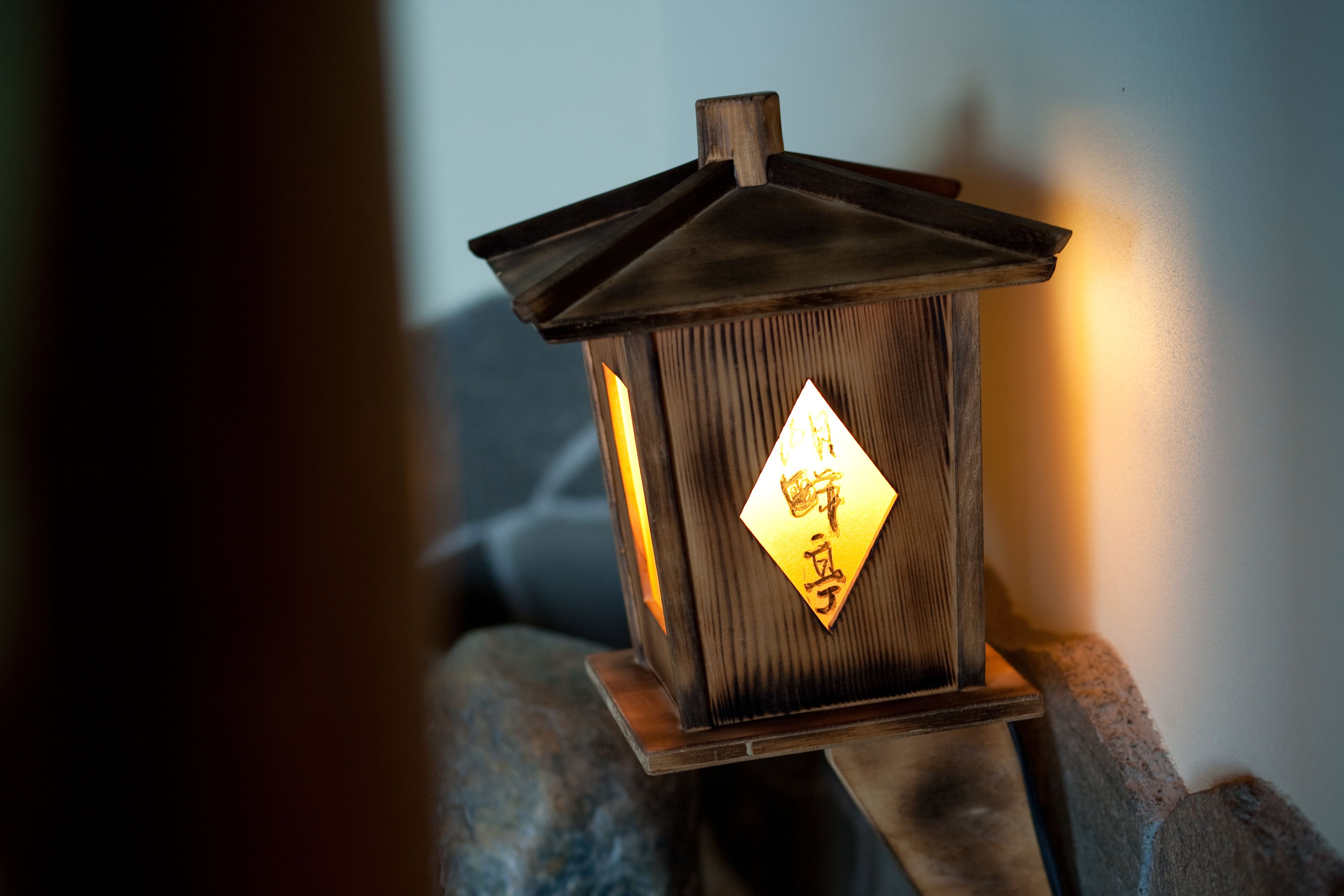 A wooden lantern with a diamond-shaped sign, placed on a stone ledge.