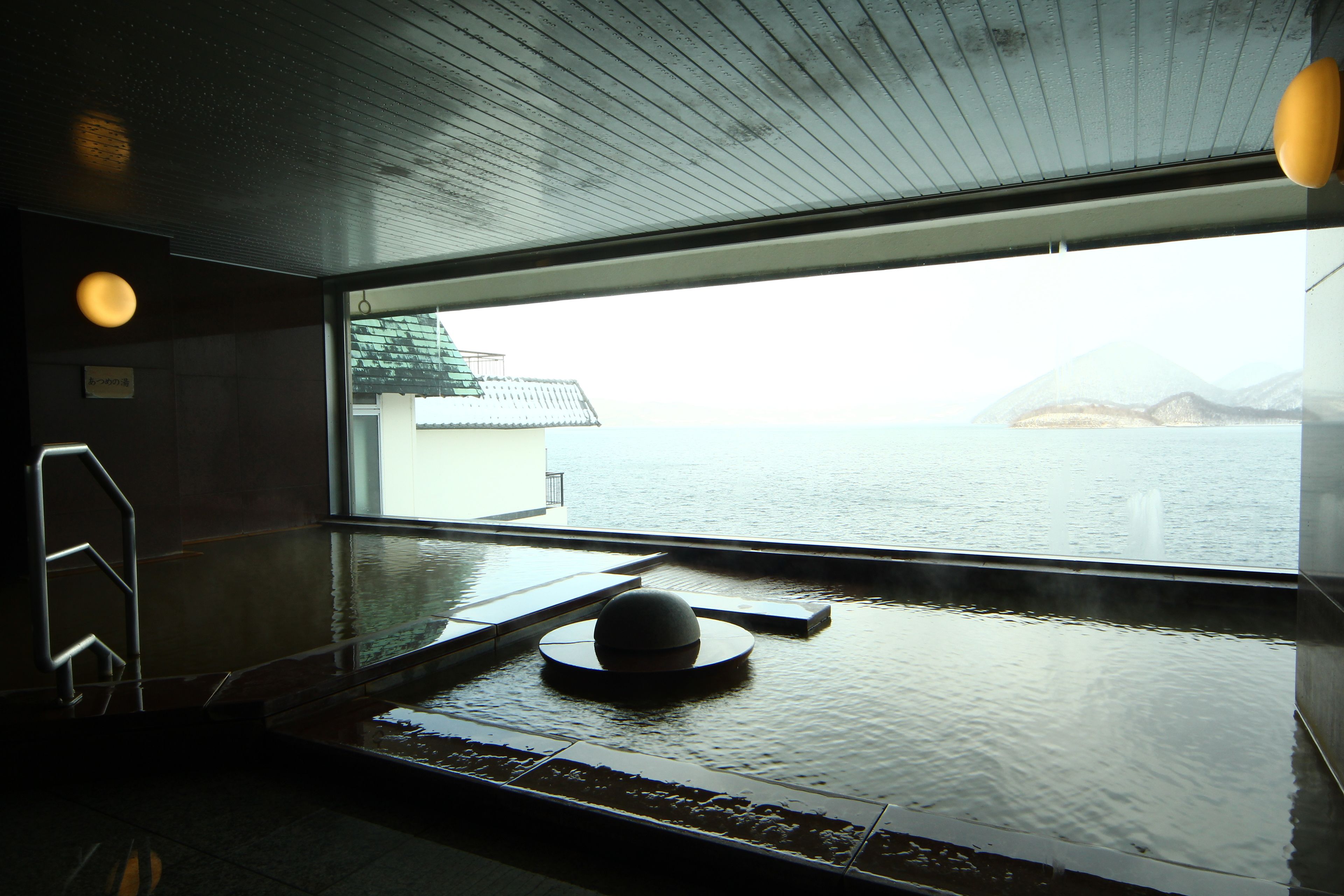 An indoor pool area with a view of the sea and mountains.
