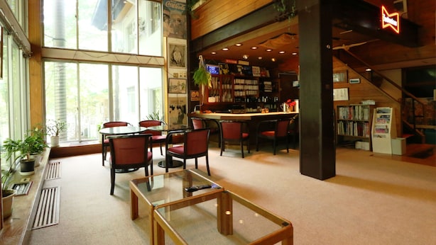 A spacious room with a large window, a bar area with bookshelves, and a staircase. - Pension ULLR (Hakuba)