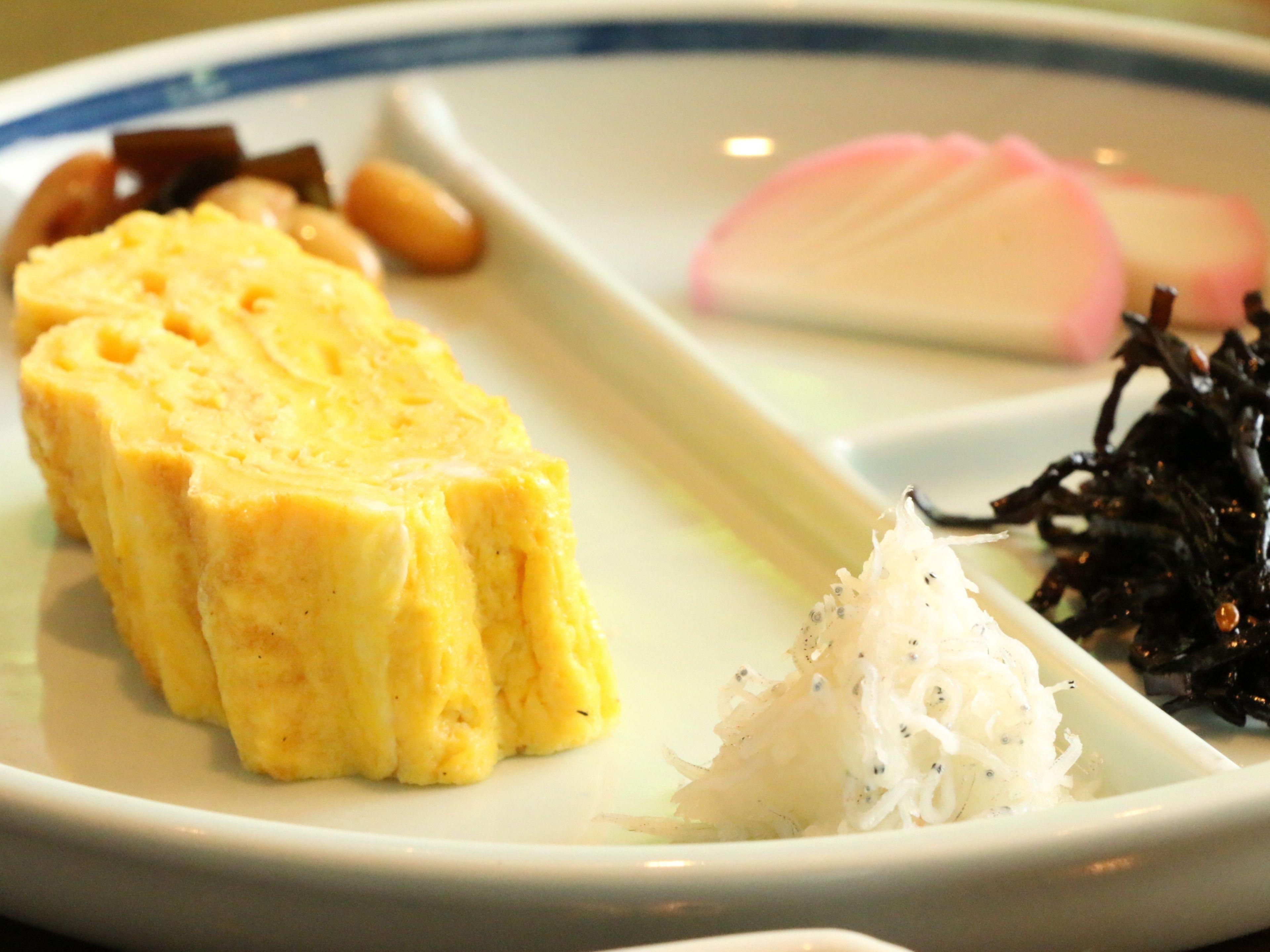 A plate with a slice of yellow cake, a piece of white fish, and some seaweed.