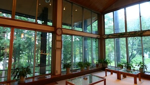 A spacious room with large windows, wooden ceiling, and multiple potted plants. - Pension ULLR (Hakuba)