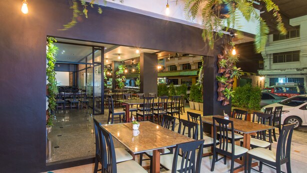 An indoor restaurant with multiple tables and chairs, surrounded by indoor plants and a glass wall. - Amity Poshtel - Hostel (Krabi)